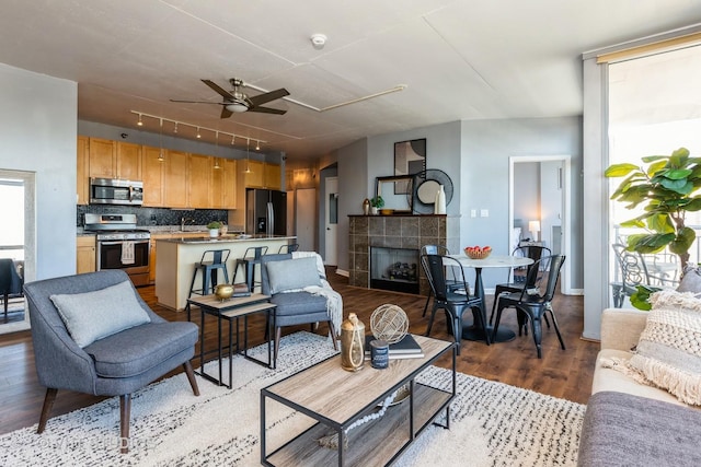 living room with ceiling fan, a tiled fireplace, and light hardwood / wood-style floors