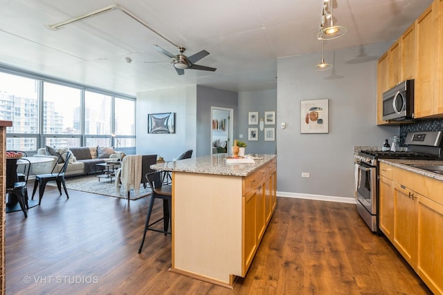 kitchen with dark wood-type flooring, appliances with stainless steel finishes, hanging light fixtures, a kitchen island, and a kitchen bar