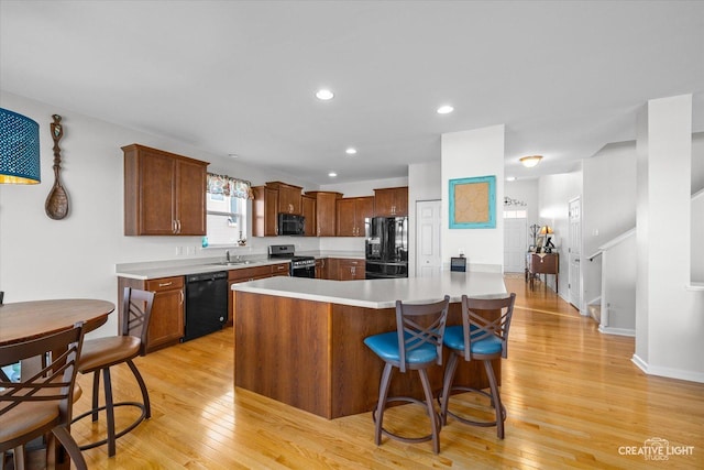 kitchen featuring sink, a breakfast bar, a kitchen island, black appliances, and light wood-type flooring