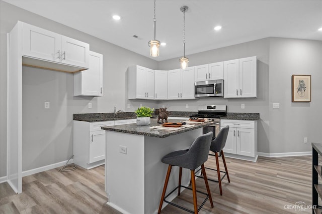 kitchen with a center island, appliances with stainless steel finishes, decorative light fixtures, light hardwood / wood-style floors, and white cabinetry