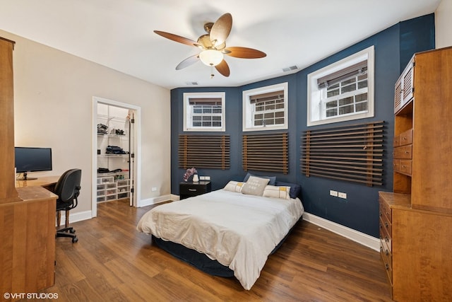 bedroom with baseboards, visible vents, a walk in closet, and wood finished floors