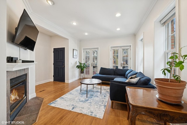 living room with baseboards, a tiled fireplace, wood finished floors, crown molding, and french doors