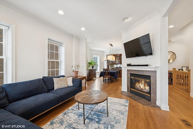 living room featuring visible vents, a tiled fireplace, light wood-style flooring, and crown molding