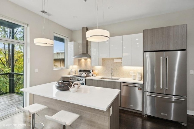 kitchen featuring stainless steel appliances, sink, wall chimney range hood, decorative light fixtures, and white cabinets