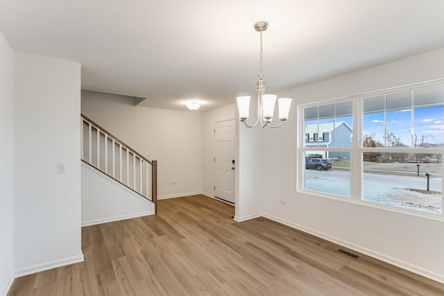 unfurnished dining area with wood-type flooring and an inviting chandelier