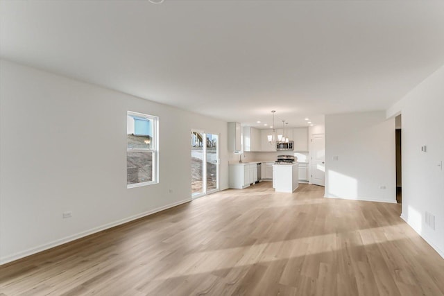 unfurnished living room featuring sink, a chandelier, and light hardwood / wood-style floors