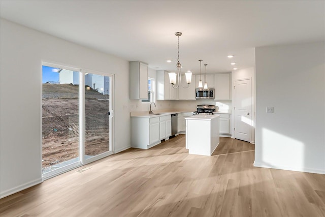 kitchen with a center island, appliances with stainless steel finishes, decorative light fixtures, white cabinets, and light wood-type flooring