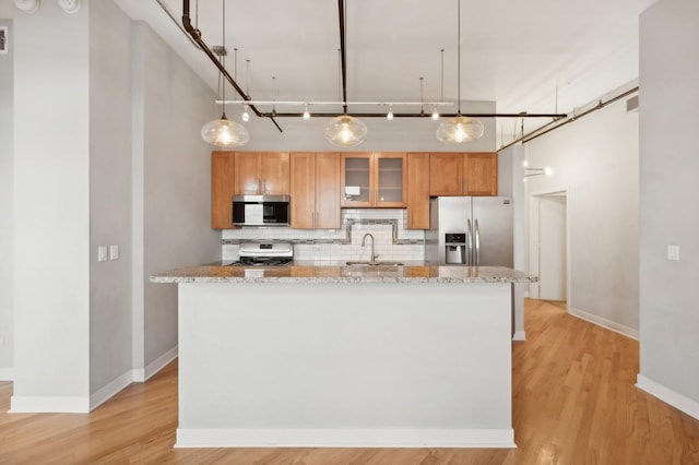 kitchen with light stone countertops, sink, hanging light fixtures, stainless steel appliances, and decorative backsplash