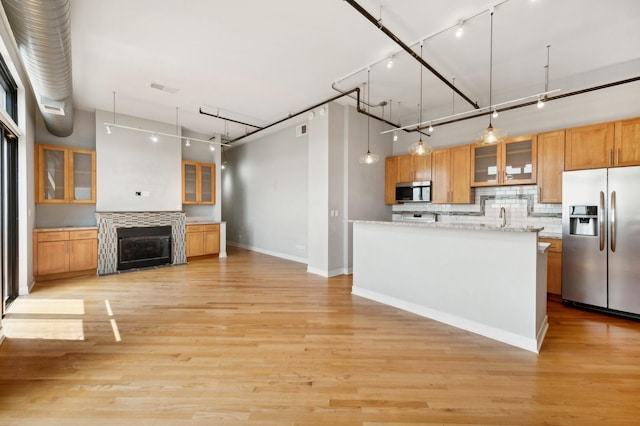 kitchen with a fireplace, appliances with stainless steel finishes, decorative light fixtures, light hardwood / wood-style floors, and light stone counters