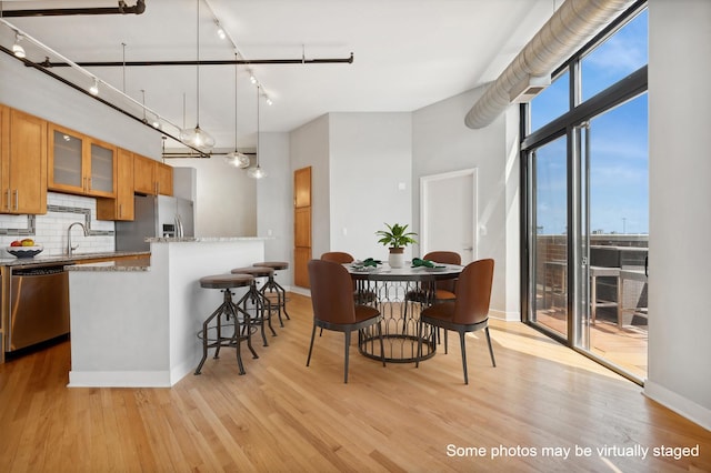 kitchen featuring backsplash, light stone counters, stainless steel appliances, decorative light fixtures, and light hardwood / wood-style floors