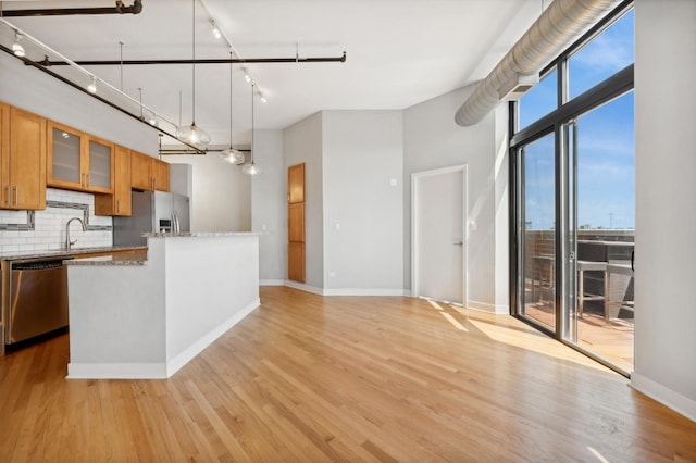 kitchen with stainless steel appliances, light stone counters, light hardwood / wood-style flooring, backsplash, and decorative light fixtures