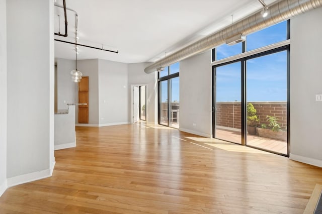 empty room with floor to ceiling windows and light hardwood / wood-style flooring