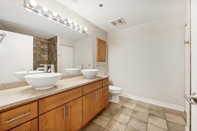 bathroom with toilet, tile patterned flooring, vanity, and tiled shower