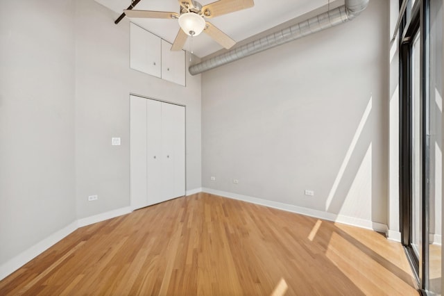 unfurnished bedroom with a closet, ceiling fan, hardwood / wood-style floors, and a towering ceiling