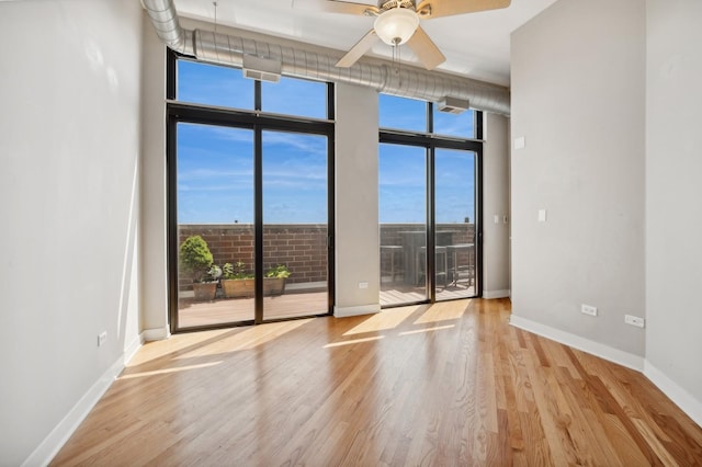 spare room with ceiling fan, expansive windows, and light wood-type flooring