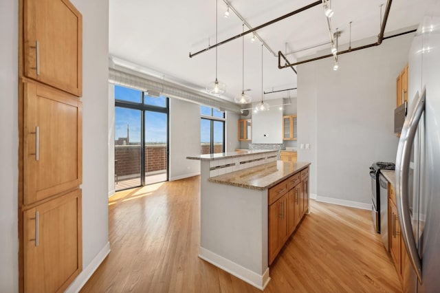 kitchen with light stone countertops, a center island, decorative light fixtures, and light wood-type flooring