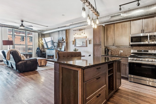 kitchen featuring pendant lighting, a center island, dark wood-type flooring, appliances with stainless steel finishes, and dark stone counters