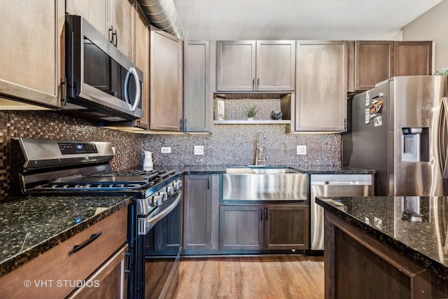 kitchen featuring sink, light hardwood / wood-style flooring, stainless steel appliances, and dark stone counters