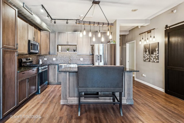 kitchen featuring stainless steel appliances, a kitchen breakfast bar, dark stone countertops, hanging light fixtures, and a kitchen island