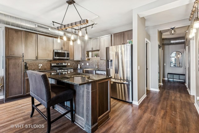 kitchen with a kitchen island, decorative light fixtures, a kitchen bar, stainless steel appliances, and dark stone countertops