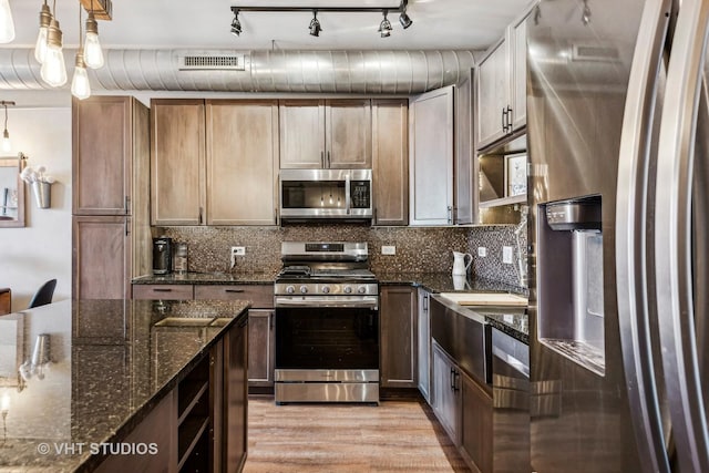 kitchen featuring decorative light fixtures, tasteful backsplash, dark stone countertops, light hardwood / wood-style flooring, and appliances with stainless steel finishes