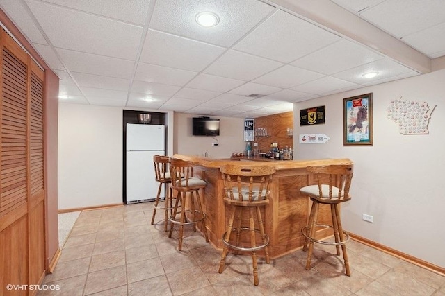 bar featuring a dry bar, baseboards, a paneled ceiling, and freestanding refrigerator