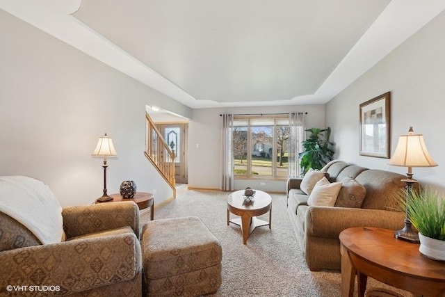 living area with a raised ceiling, light carpet, baseboards, and stairs