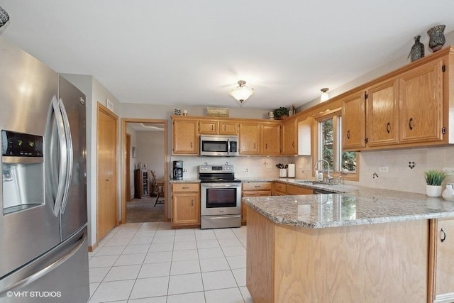 kitchen with light stone counters, light tile patterned floors, stainless steel appliances, a sink, and a peninsula