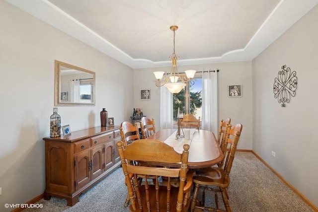 dining room featuring dark carpet, a raised ceiling, an inviting chandelier, and baseboards