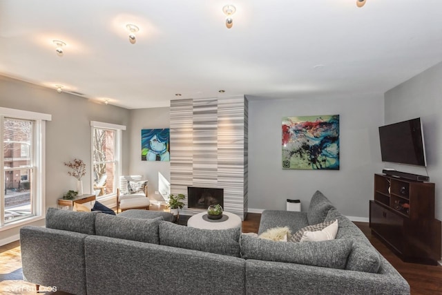 living room featuring dark wood-style flooring, a tile fireplace, and baseboards