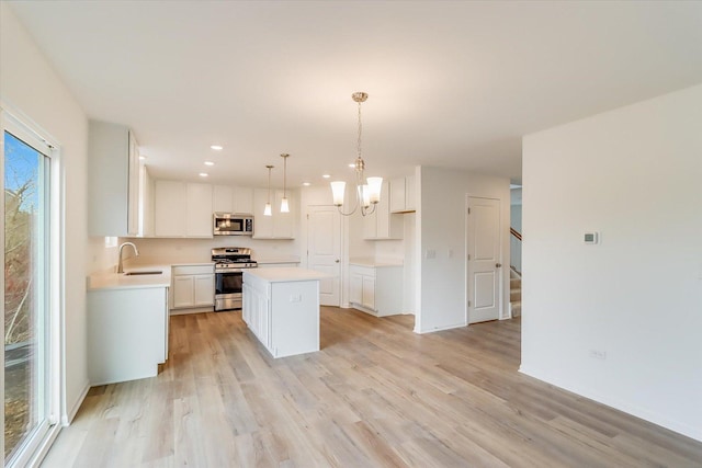 kitchen with decorative light fixtures, a center island, light wood-type flooring, appliances with stainless steel finishes, and white cabinets