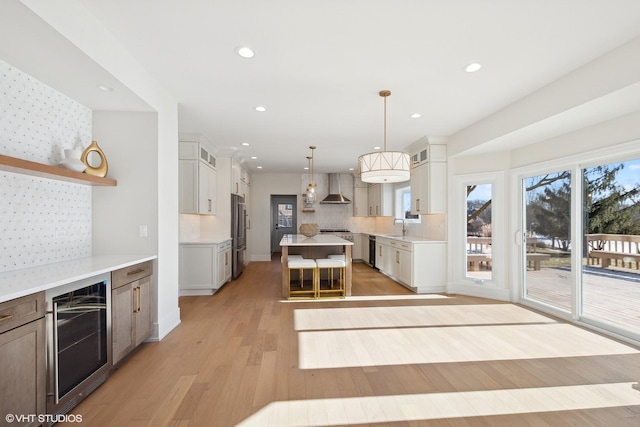 kitchen featuring pendant lighting, white cabinetry, wine cooler, a center island, and wall chimney range hood