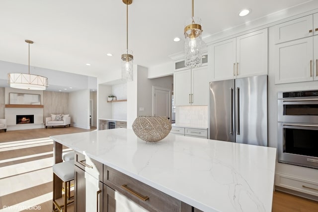 kitchen with tasteful backsplash, appliances with stainless steel finishes, white cabinets, and decorative light fixtures