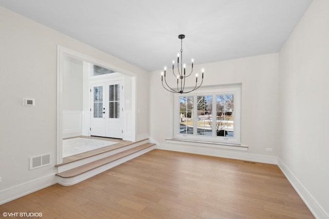 unfurnished dining area with a chandelier, light hardwood / wood-style floors, and french doors