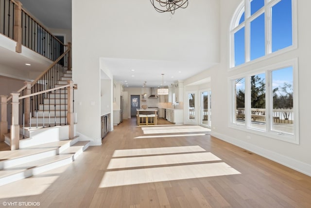 unfurnished living room featuring an inviting chandelier, sink, light hardwood / wood-style floors, and a high ceiling