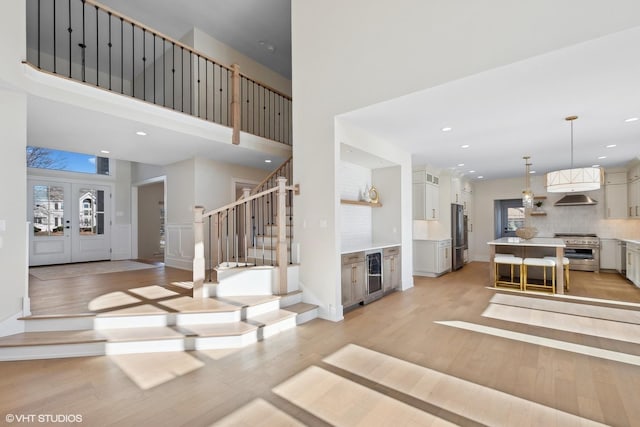 living room featuring wine cooler, light hardwood / wood-style floors, and a high ceiling