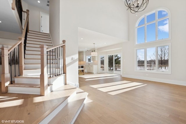 entrance foyer featuring a towering ceiling, a chandelier, and light wood-type flooring