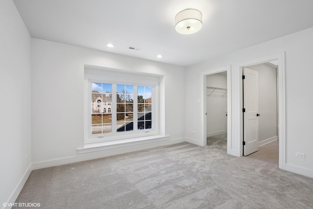 unfurnished bedroom featuring a spacious closet, light carpet, and a closet