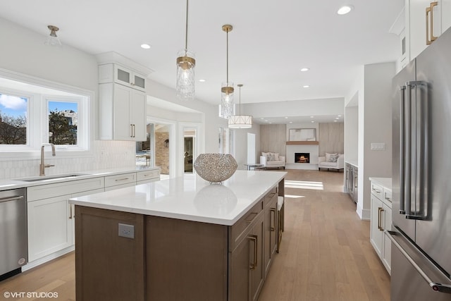 kitchen with appliances with stainless steel finishes, pendant lighting, white cabinetry, sink, and a center island