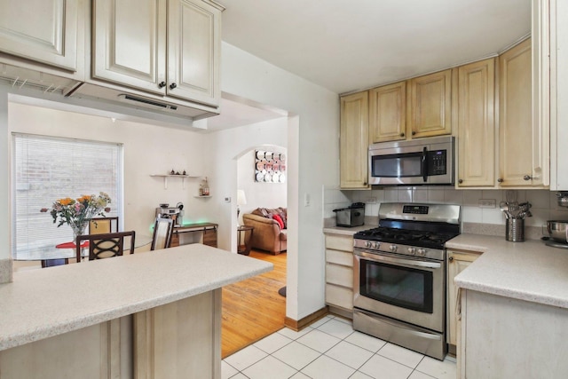 kitchen with stainless steel appliances, cream cabinetry, light tile patterned floors, and tasteful backsplash