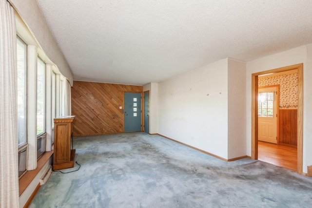 unfurnished living room featuring a textured ceiling, light colored carpet, and wooden walls