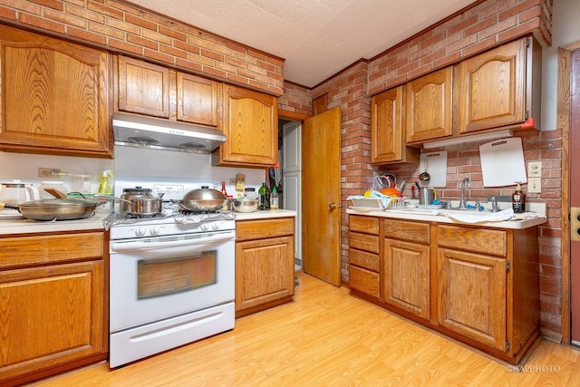 kitchen featuring sink, light hardwood / wood-style floors, white range with gas cooktop, and brick wall