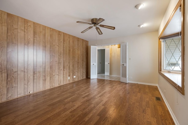 unfurnished room with ceiling fan, wood walls, and dark wood-type flooring