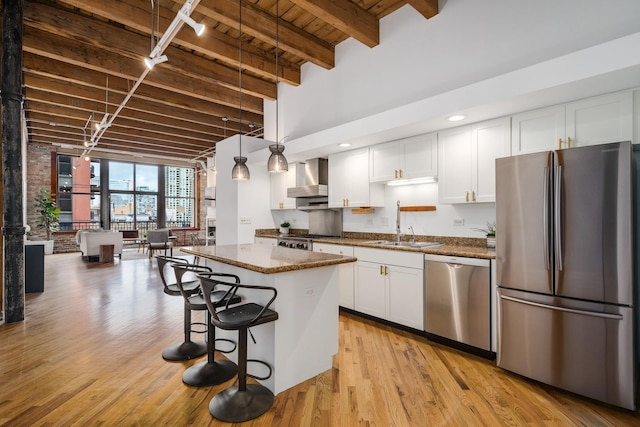 kitchen featuring white cabinets, appliances with stainless steel finishes, a center island, wall chimney exhaust hood, and decorative light fixtures