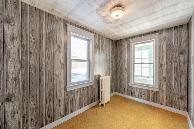 spare room featuring light carpet, plenty of natural light, radiator, and wood walls