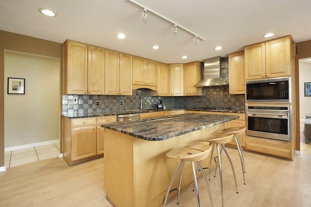 kitchen featuring light brown cabinets, wall chimney range hood, and appliances with stainless steel finishes