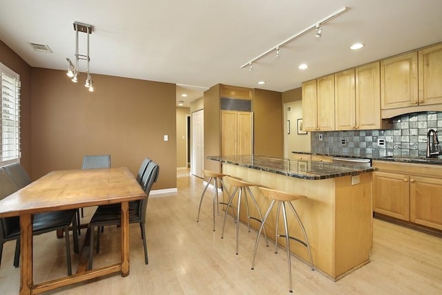 kitchen with sink, hanging light fixtures, dark stone countertops, light hardwood / wood-style floors, and a kitchen island