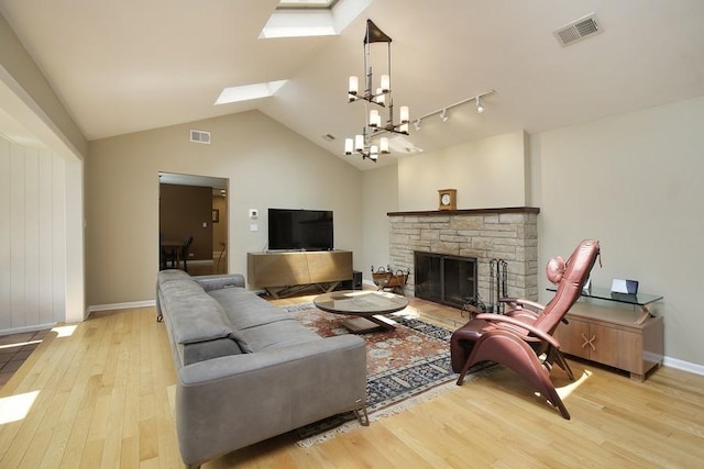 living room with vaulted ceiling with skylight, a stone fireplace, light wood-type flooring, and an inviting chandelier