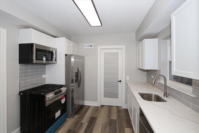 kitchen with light stone countertops, white cabinetry, sink, stainless steel appliances, and backsplash