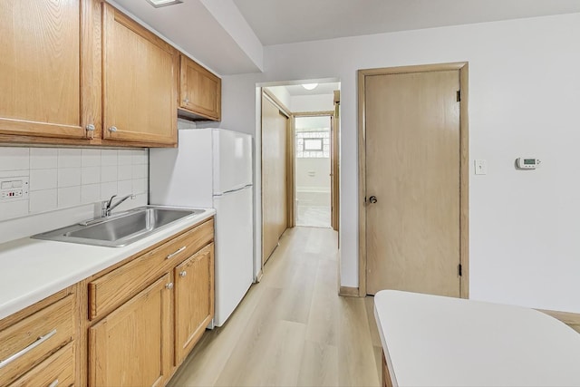 kitchen featuring backsplash, light hardwood / wood-style floors, white refrigerator, and sink